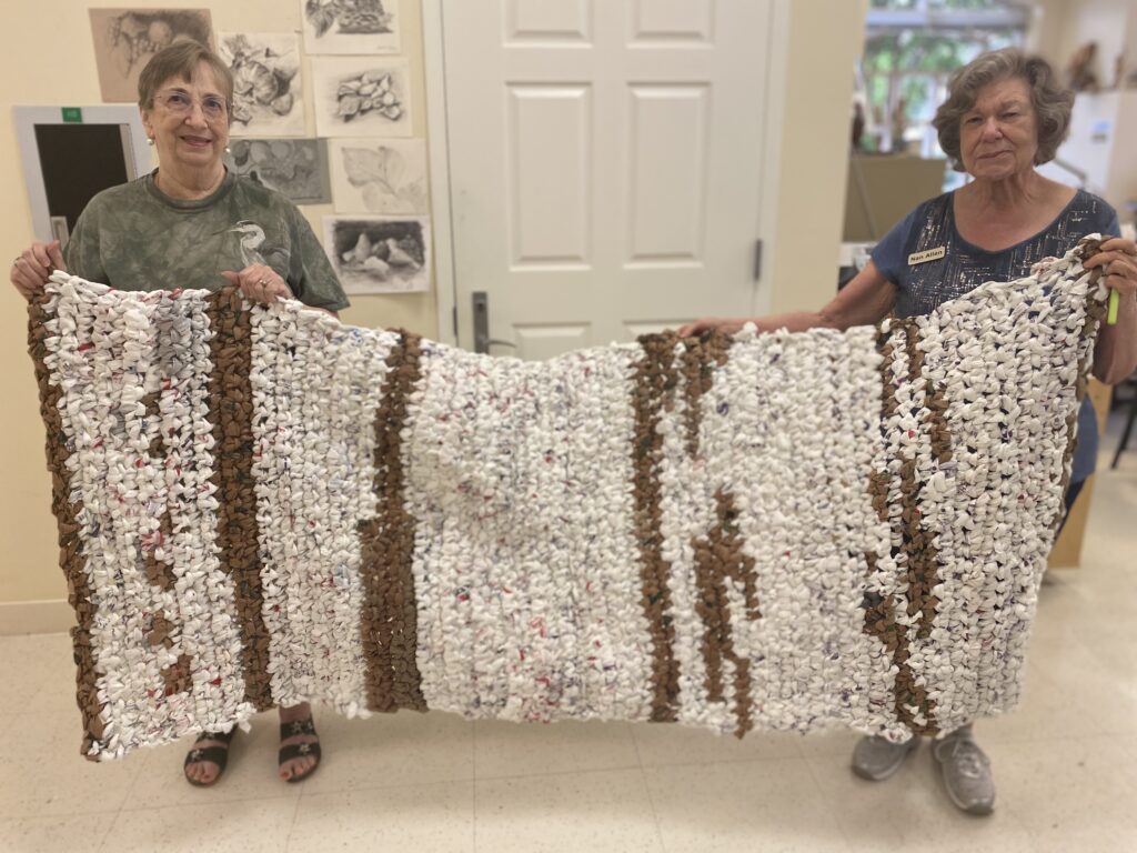Trude Myers (left) and Nan Allen (right) hold one of the completed plarn mats.